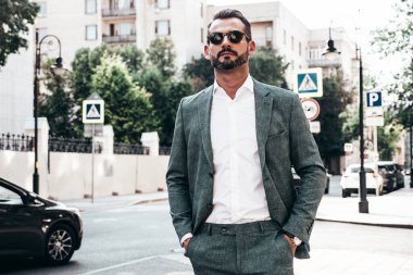 Yakışıklı, kendine güvenen, stil sahibi, lamberseksüel bir modelin portresi. Zarif takım elbise giymiş modern bir adam. Moda erkeği gün batımında Avrupa şehrinin arka planında poz veriyor. Güneş gözlükleriyle