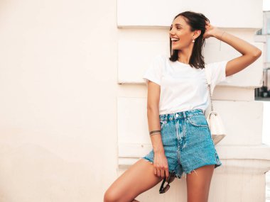 Güzel gülümseyen hippi bir kadının son moda kot şortlu portresi. Günbatımında sokakta poz veren kaygısız seksi manken. Güneş gözlüklü pozitif model.