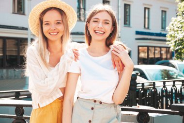 Son moda yaz kıyafetleri içinde iki güzel gülümseyen yeniyetme kadın. Sokakta şapkalı kayla poz veren kaygısız kadınlar. Pozitif saf modeller gün batımında eğleniyorlar, sarılıyorlar. 
