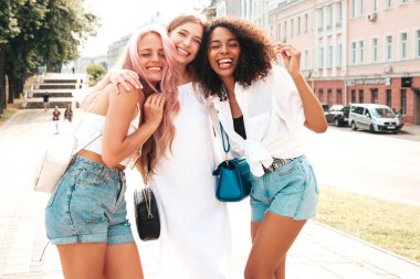 Son moda yaz kıyafetleri içinde üç güzel gülümseyen hippi kadın. Sokakta poz veren tasasız, çok ırklı kadınlar. Güneş gözlükleriyle eğlenen pozitif modeller. Neşeli ve mutlu