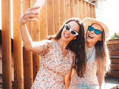 Son moda yaz kıyafetleri içinde iki güzel gülümseyen yeniyetme kadın. Sokakta şapkalı kayla poz veren kaygısız kadınlar. Pozitif saf modeller gün batımında eğleniyorlar, sarılıyorlar. Selfie çekiyoruz.