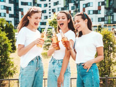 Üç güzel, güler yüzlü yeniyetme kadın aynı yaz kıyafetleri içinde. Sokakta poz veren kaygısız kadınlar. Güneş gözlükleriyle eğlenen pozitif modeller. Şişe bira içmek. Ekim Festivali