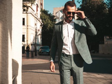 Yakışıklı, kendine güvenen, stil sahibi, lamberseksüel bir modelin portresi. Zarif takım elbise giymiş modern bir adam. Moda erkeği gün batımında Avrupa şehrinin arka planında poz veriyor. Güneş gözlükleriyle