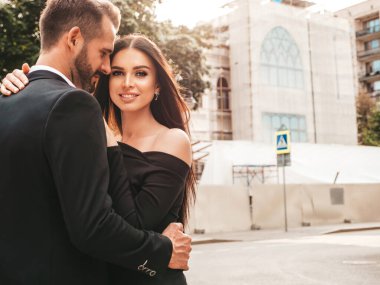 Güzel moda kadını ve takım elbiseli yakışıklı erkek arkadaşı. Siyah gece elbisesi içinde seksi, gülümseyen esmer manken. Günbatımında sokakta poz veren şık bir çift. Vahşi adam ve dişisi açık havada