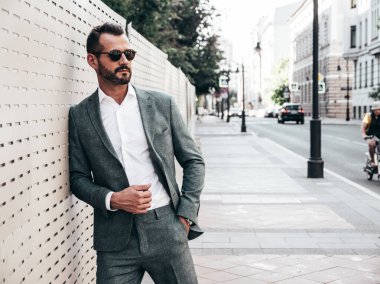 Yakışıklı, kendine güvenen, stil sahibi, lamberseksüel bir modelin portresi. Zarif takım elbise giymiş modern bir adam. Moda erkeği gün batımında Avrupa şehrinin arka planında poz veriyor. Güneş gözlükleriyle