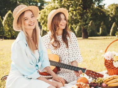 İki güzel hippi kadın, son moda yaz elbisesi ve şapkaları içinde. Kaygısız kadınlar dışarıda piknik yapıyor. Çimlerin üzerinde oturan, meyve ve peynir yiyen pozitif modeller. Gitar çalıyorum.