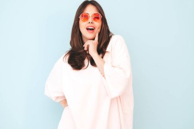 Son moda pembe giysiler içinde gülümseyen güzel bir kadının portresi. Stüdyoda açık mavi duvarın yanında poz veren kaygısız seksi kadın. Pozitif model içeride eğleniyor. Neşeli ve mutlu 