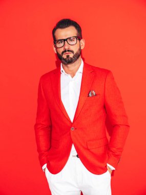 Yakışıklı, kendine güvenen, stil sahibi hipster Lambersex modelinin portresi. Zarif takım elbiseli seksi modern adam. Gözlüklü, kırmızı duvarın yanındaki stüdyoda poz veren modacı erkek.
