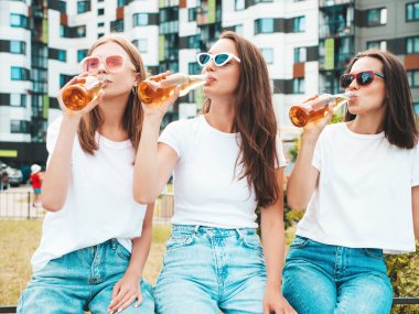 Üç güzel, güler yüzlü yeniyetme kadın aynı yaz kıyafetleri içinde. Sokakta poz veren kaygısız kadınlar. Güneş gözlükleriyle eğlenen pozitif modeller. Şişe bira içmek. Ekim Festivali