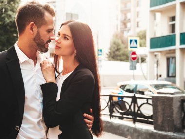 Güzel moda kadını ve takım elbiseli yakışıklı erkek arkadaşı. Siyah gece elbisesi içinde seksi, gülümseyen esmer manken. Günbatımında sokakta poz veren şık bir çift. Vahşi adam ve dişisi açık havada