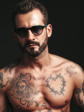 Yakışıklı, kendine güvenen, stil sahibi hipster Lambersex modelinin portresi. Seksi, modern adam. Dövmeli çıplak gövde. Stüdyoda siyah arka planda poz veren moda erkek. Güneş gözlükleriyle