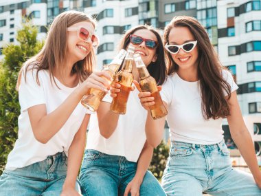 Üç güzel, güler yüzlü yeniyetme kadın aynı yaz kıyafetleri içinde. Sokakta poz veren kaygısız kadınlar. Güneş gözlükleriyle eğlenen pozitif modeller. Şişe bira içmek. Ekim Festivali