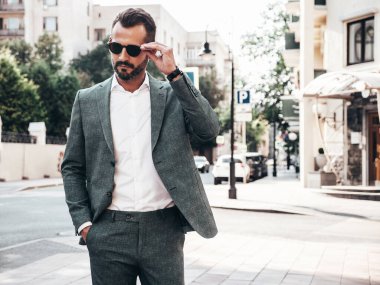 Yakışıklı, kendine güvenen, stil sahibi, lamberseksüel bir modelin portresi. Zarif takım elbise giymiş modern bir adam. Moda erkeği gün batımında Avrupa şehrinin arka planında poz veriyor. Güneş gözlükleriyle