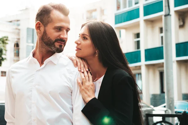 Beautiful fashion woman and her handsome elegant boyfriend in suit. Sexy brunette model in black evening dress. Fashionable couple posing in the street in Europe. Brutal man and his female outdoors