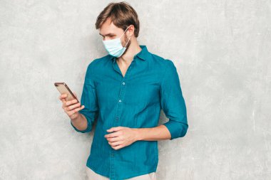 Yakışıklı, güler yüzlü hippi, keresteci iş adamı mankeni, günlük kot gömlek giyiyor. Moda adamı stüdyoda duvarın yanında poz veriyor. Cep telefonu ekranına bakıyor, uygulamalar kullanıyor. Koruyucu tıbbi maskeyle