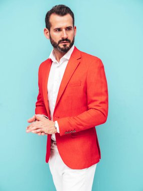 Yakışıklı, kendine güvenen, stil sahibi, lamberseksüel modelin portresi. Zarif kırmızı takım elbise giymiş modern bir adam. Moda erkeği stüdyoda mavi duvarın yanında poz veriyor. 