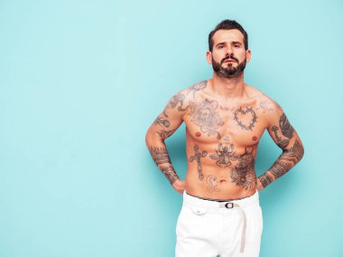 Yakışıklı, kendine güvenen, stil sahibi hipster Lambersex modelinin portresi. Seksi, modern adam. Dövmeli çıplak gövde. Moda erkeği stüdyoda açık mavi duvarın yanında poz veriyor.