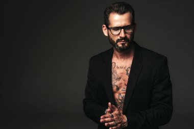 Yakışıklı, kendine güvenen, stil sahibi hipster Lambersex modelinin portresi. Siyah ceket giyen seksi modern adam. Dövmeli çıplak gövde. Stüdyoda siyah arka planda poz veren moda erkek. Gözlüklerle