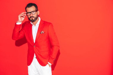 Yakışıklı, kendine güvenen, stil sahibi hipster Lambersex modelinin portresi. Zarif takım elbiseli seksi modern adam. Gözlüklü, kırmızı duvarın yanındaki stüdyoda poz veren modacı erkek.