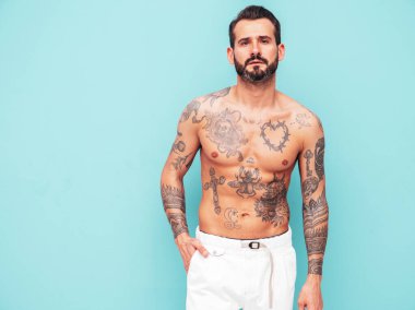 Yakışıklı, kendine güvenen, stil sahibi hipster Lambersex modelinin portresi. Seksi, modern adam. Dövmeli çıplak gövde. Moda erkeği stüdyoda açık mavi duvarın yanında poz veriyor.
