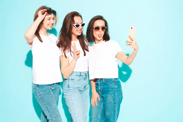 三个年轻美丽的嬉皮士女 穿着时髦的夏天白色T恤和牛仔裤衣服 性感无忧无虑的女人在浅蓝色的墙壁附近摆姿势学习 快乐而积极的模特自拍 — 图库照片