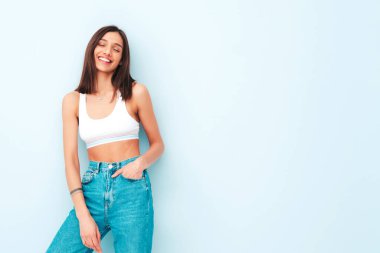 Beyaz formalı bluz ve kot pantolon giymiş güzel bir kadın. Seksi kaygısız neşeli model sabahının tadını çıkarıyor. Şirin ve pozitif kadın stüdyoda açık mavi duvarın yanında poz veriyor.