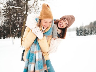 Son moda sıcak kıyafetler ve eşarplar içinde iki güzel, gülümseyen hippi kadın. Parktaki sokakta poz veren tasasız kadınlar. Pozitif saf modeller karda eğleniyor. Kış anlarının tadını çıkarıyorum. Xmas kavramı