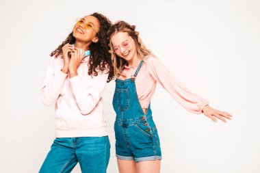 İki güzel gülümseyen uluslararası hippi kadın moda yaz kıyafetleri içinde. Stüdyoda gri arka planda poz veren kaygısız kadınlar. Olumlu modeller eğleniyor.