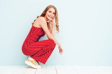 Yeni moda kırmızı takım elbiseli güzel, gülümseyen bir kadının portresi. Stüdyoda açık mavi duvarın yanında poz veren kaygısız seksi kadın. Pozitif model içeride eğleniyor. Neşeli ve mutlu