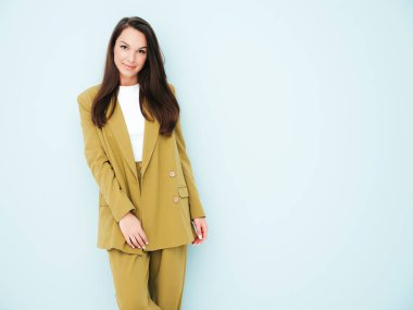 Moda kıyafetleri içinde gülümseyen genç ve güzel bir bayan. Stüdyoda açık mavi duvarın yanında poz veren kaygısız seksi kadın. Pozitif model içeride eğleniyor. Neşeli ve mutlu