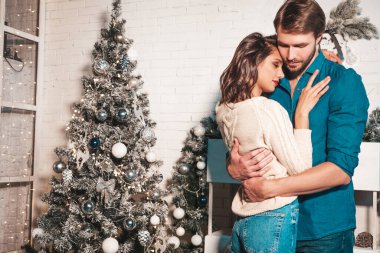 Gülümseyen güzel kadın ve yakışıklı erkek arkadaşı. Mutlu neşeli aile Noel ağacının yanında beyaz iç kısımda poz veriyor. Mankenler sarılıyor. Aşk, Noel konsepti