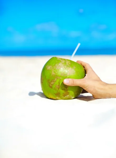 Coco con la mano de la persona en la arena blanca de la playa cerca del océano en el día soleado del verano —  Fotos de Stock