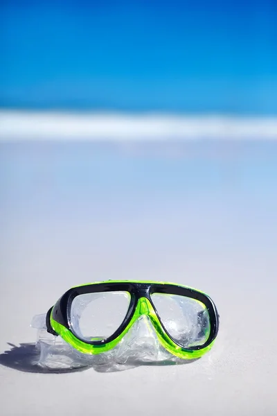 Green snorkel and waterproof mask lying on sand behind blue sky and ocean