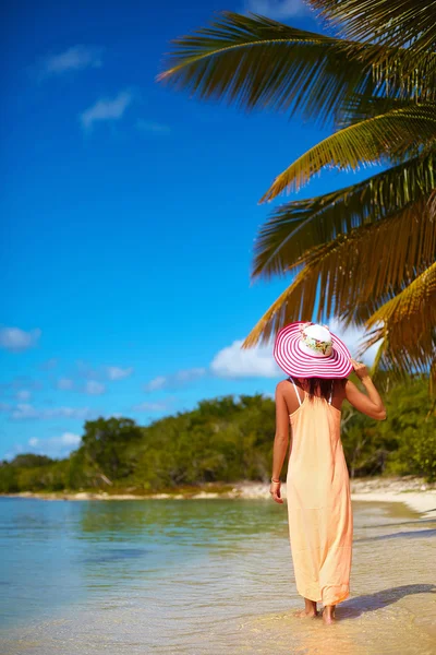 Hot beautiful woman in colorful sunhat and dress walking near beach ocean on hot summer day near palm — Stock Photo, Image