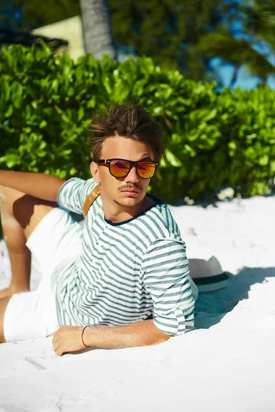 Stylish young male model man lying on beach sand  wearing hipster summer hat  enjoying summer travel holiday near ocean in sunglasses — Stock Photo, Image