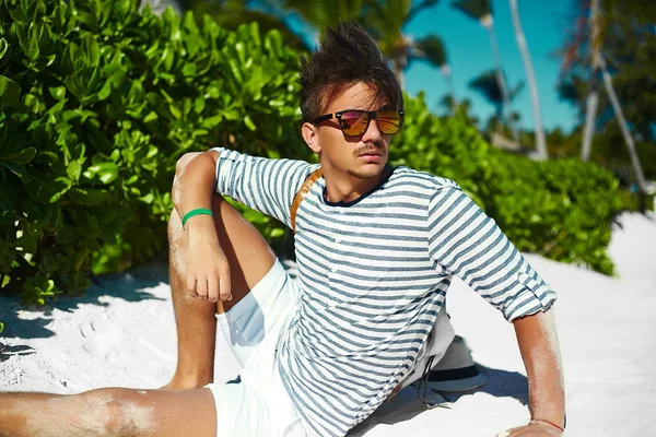 Stylish young male model man lying on beach sand  wearing hipster summer hat  enjoying summer travel holiday near ocean in sunglasses — Stock Photo, Image