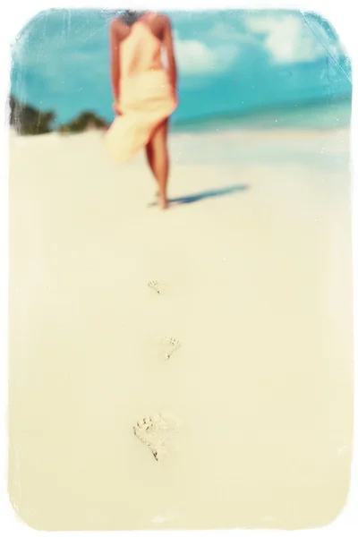 Foto retro vintage de mujer en vestido colorido caminando en el océano de playa dejando huellas en la arena —  Fotos de Stock