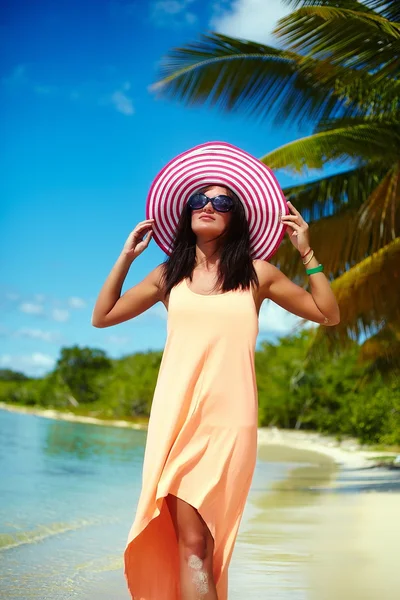 Hot beautiful woman in colorful sunhat and dress walking near beach ocean on hot summer day near palm — Stock Photo, Image