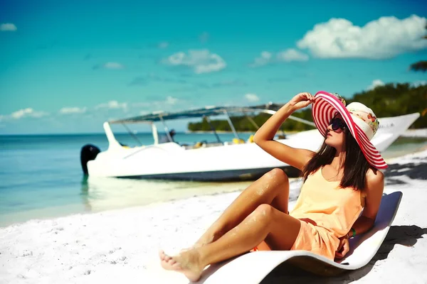 Beautiful woman model sunbathing on the beach chair in white bikini in colorful sunhat behind blue summer water ocean — Stock Photo, Image