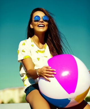Funny crazy glamor stylish sexy smiling beautiful young woman model in  bright hipster summer casual cloth with colorful ball in the street behind blue sky