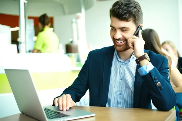 Young fashion smiling hipster man  in the city cafe during lunch time with notebook in suit speaking on phone — Stockfoto