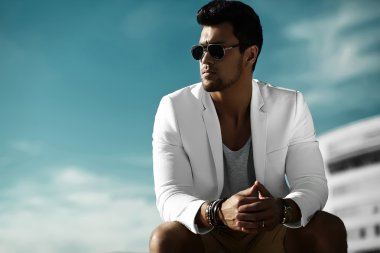 Genç seksi işadamı yakışıklı modeli erkek güneş gözlüğü mavi gökyüzü arkasındaki sokakta sıradan bez elbiseli moda portre