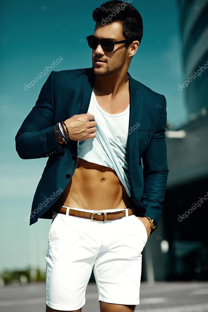 Fashion portrait of young sexy businessman handsome muscled  model man in casual cloth suit in sunglasses in the street showing his  abdominal muscles