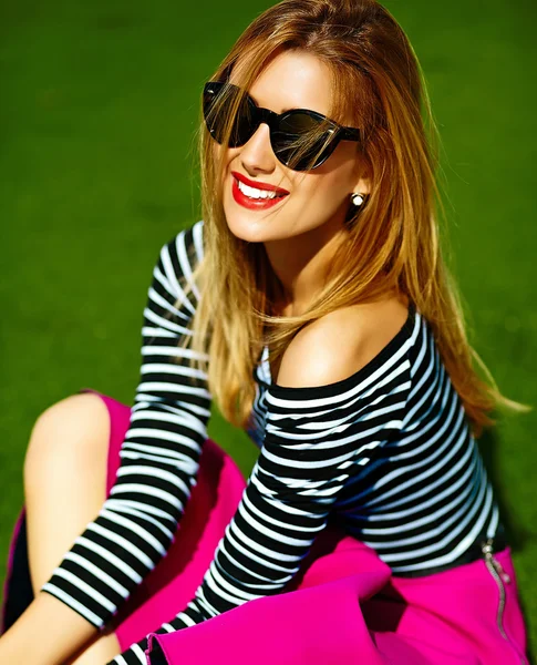 Смешной сумасшедший гламур стильная сексуальная улыбающаяся красивая блондинка модель в розовой хипстерской одежде сидя в траве в парке — стоковое фото