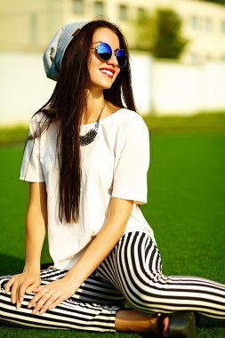 Funny crazy glamor stylish sexy smiling beautiful  young woman model in hipster clothes in beanie sitting in the grass in the park