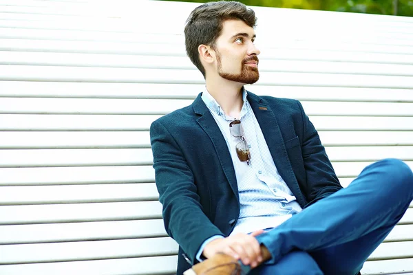 Jovem hipster bonito Estudante Masculino Sentado no banco em um parque de terno — Fotografia de Stock