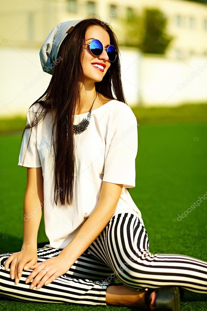 Funny crazy glamor stylish sexy smiling beautiful  young woman model in hipster clothes in beanie sitting in the grass in the park