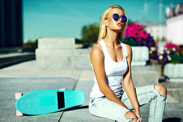 Alta moda look.glamor elegante sexy bela jovem loira modelo menina no verão brilhante casual hipster roupas com skate sentado na rua — Fotografia de Stock