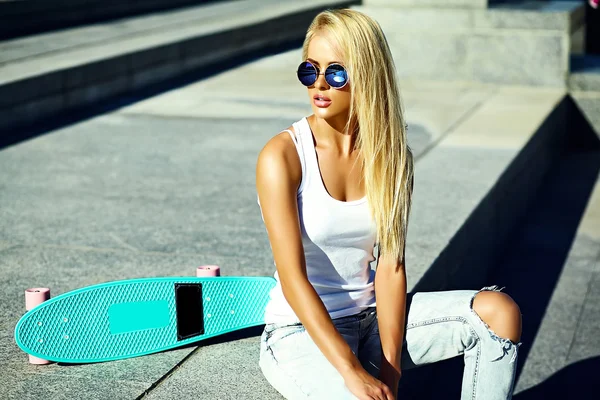 High fashion look.glamor stylish sexy beautiful young blond  model girl in summer bright casual hipster clothes with skateboard sitting in the street — Zdjęcie stockowe