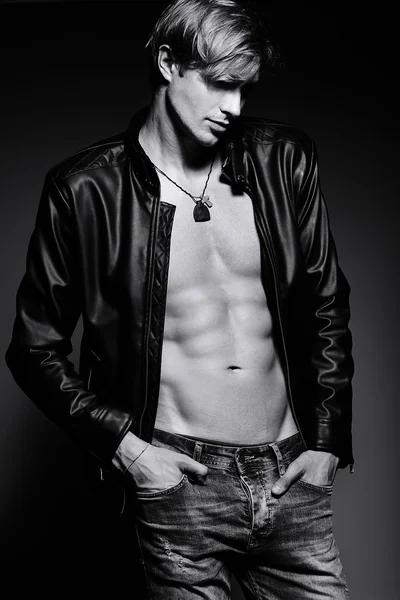 Young handsome muscled fit male model man in leather jacket posing in studio showing his abdominal muscles — Stock Photo, Image